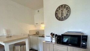 Cocina compacta con una mesa de madera, microondas, tostadora y un reloj en la pared.