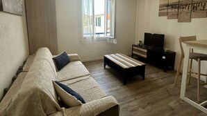 Una sala de estar con sofá, mueble para televisión, mesa de comedor y ventana con cortinas.