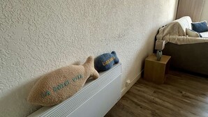 Una habitación con un radiador, una cama con manta y almohadas, y una mesita de noche de madera con lámpara.