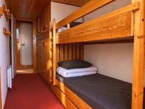 Una habitación compacta con literas de madera, suelo de moqueta roja y una puerta que da al baño.