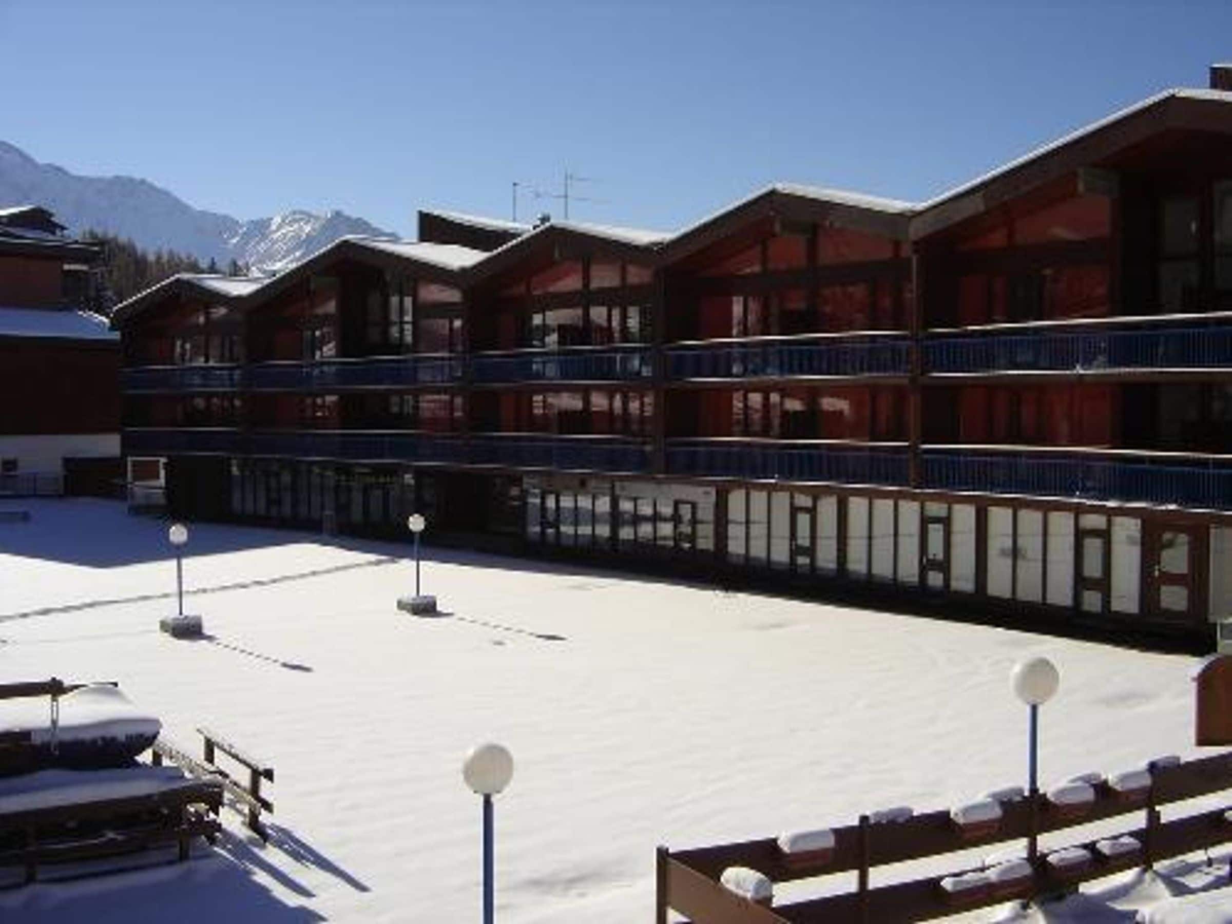A hotel with multiple balconies, a snow-covered courtyard, and a mountainous backdrop.