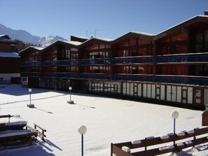 Ein Hotel mit mehreren Balkonen, einem verschneiten Innenhof und einer Bergkulisse im Hintergrund.