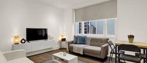 A modern living room with a flat-screen TV, a sofa, a coffee table, and a dining area with a table and chairs.