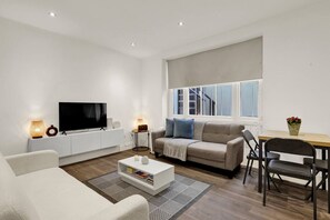 Ein modernes Wohnzimmer mit Flachbildfernseher, einer Couch, einem Couchtisch und einem Essbereich mit Tisch und Stühlen.