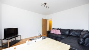 En moderne stue med et fladskærms-tv, en sort lædersofa og et træbord.