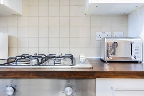 Cozinha com fogão a gás, torradeira e painel de azulejos brancos.