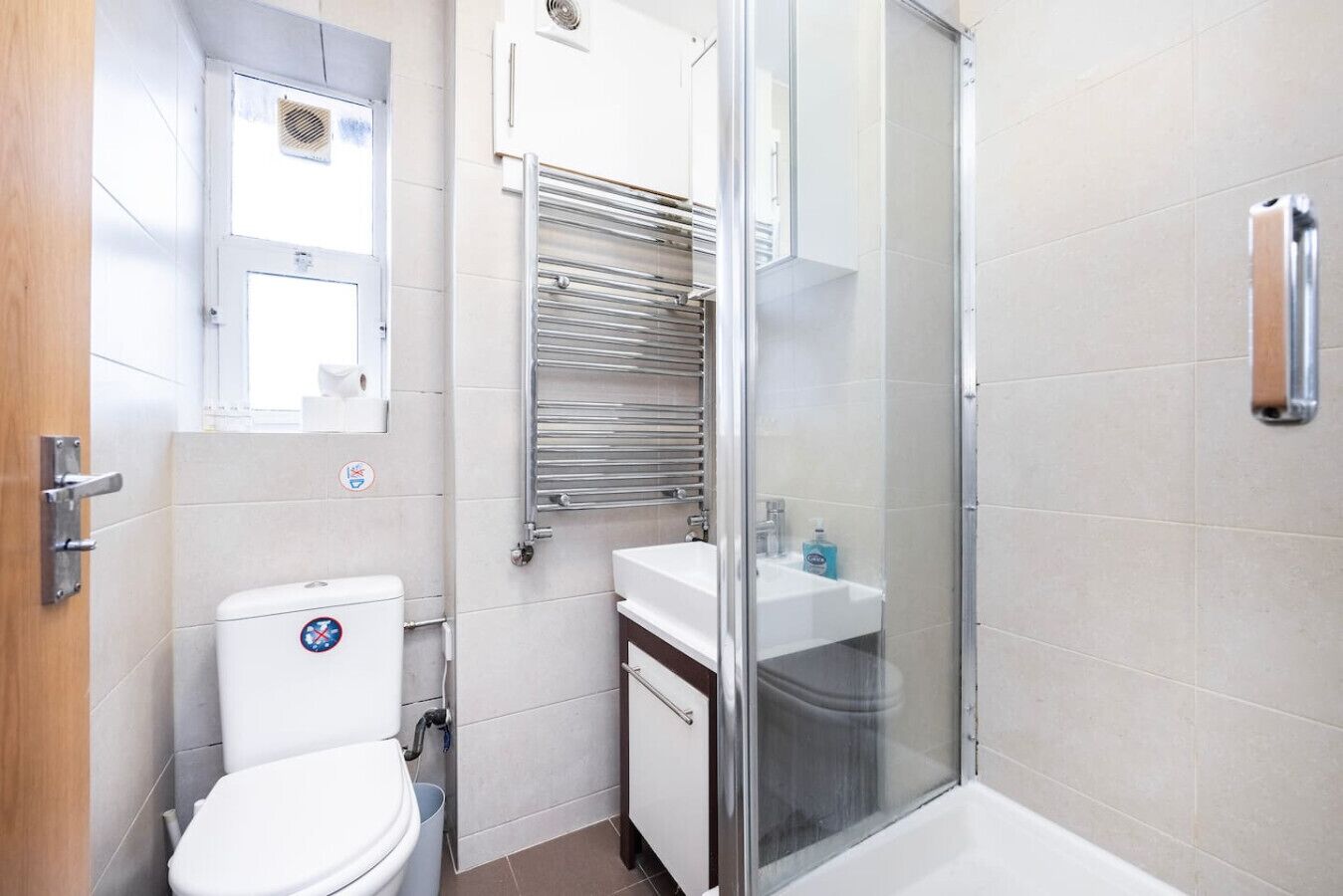 Een badkamer met toilet, wastafel, douchecabine van glas en een handdoekrek.