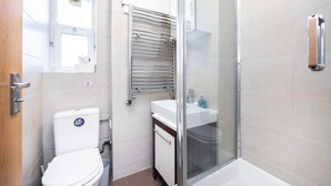 Et badeværelse med toilet, håndvask, brusekabine i glas og et håndklædestativ.