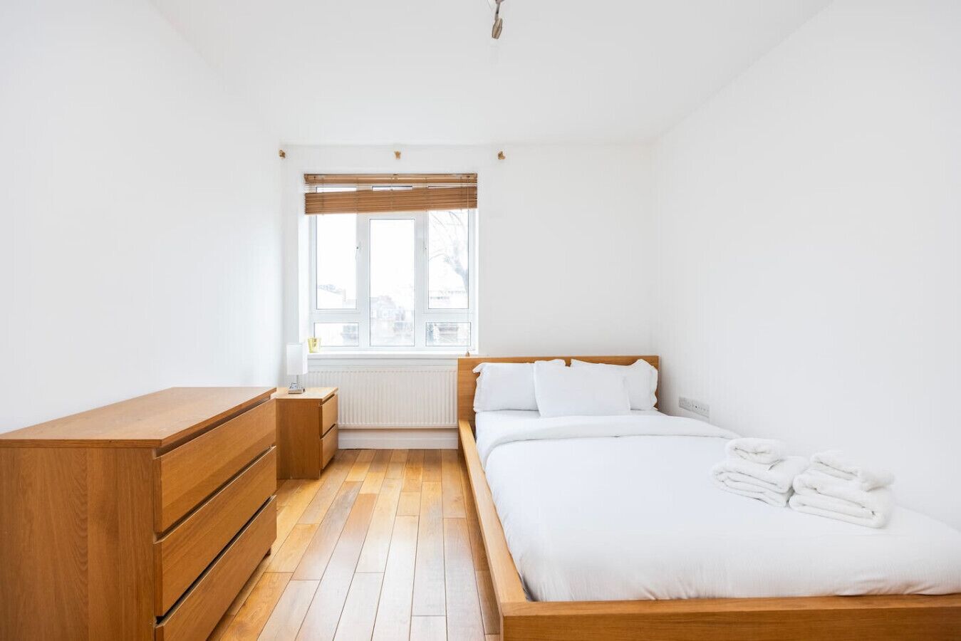A bedroom with a wooden bed, a nightstand, a dresser, and a window with blinds.