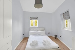 Ein Schlafzimmer mit einem Bett, zwei Fenstern, einer Heizung und einer Deckenleuchte.