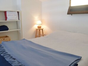 A bedroom with a bed, a lamp, a shelf with a bag, and a basket. - Studio mezzanine with sea view - 3 guests (Fleury-Saint-Pierre-la-Mer)