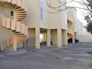 A parking lot with a spiral staircase leading to a building entrance. - Studio mezzanine with sea view - 3 guests (Fleury-Saint-Pierre-la-Mer)
