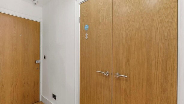 A hallway with two wooden doors, one with a lock and a keyhole, and the other with a keyhole and a small blue sticker. - 1BR in Prime Islington Location near Angel Station (Greater London)
