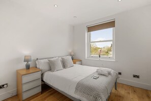 A bedroom with a bed, bedside tables, a window, and a view of greenery.