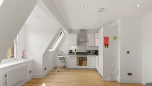 A modern kitchen with white cabinets, a dining area with a high table, and a view through a skylight. - 1BR in Prime Islington Location near Angel Station (Greater London)