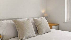 A bed with two pillows, a bedside table, a lamp, and a window. - 1BR in Prime Islington Location near Angel Station (Greater London)