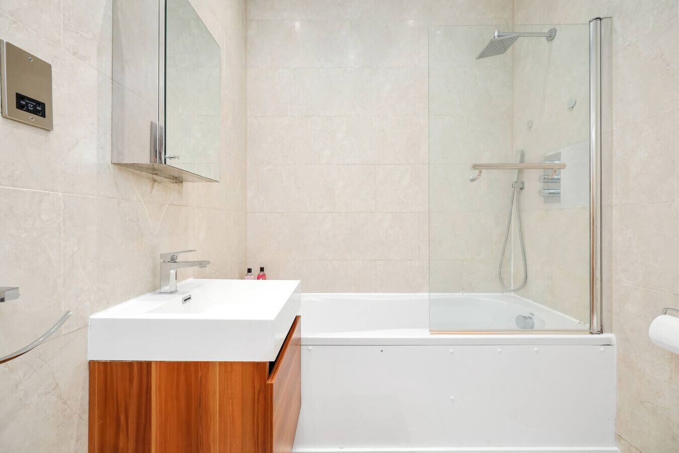 Une salle de bain moderne avec un lavabo blanc, un meuble-lavabo en bois, une douche à parois de verre et un mur recouvert de carreaux de marbre.