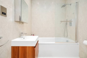 Ein modernes Badezimmer mit einem weißen Waschbecken, einer Holzausstattung, einer Duschkabine aus Glas und einer Wand mit Marmorfliesen.