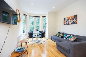 Ein modernes Wohnzimmer mit einem grauen Sofa, einem runden Tisch mit Stühlen und einem Bild an der Wand.
