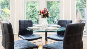 Ein Essbereich mit einem runden Glastisch, vier schwarzen Ledersesseln und einer weißen Vase mit Blumen.