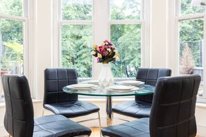 Ein Essbereich mit einem runden Glastisch, vier schwarzen Ledersesseln und einer weißen Vase mit Blumen.