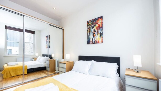 Ein modernes Hotelzimmer mit einem großen Bett, Nachttischen, einem Spiegel und einem Bild an der Wand.