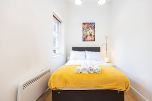 A hotel room with a bed, a window, a radiator, and a painting on the wall. - 2BR in Islington Near Highbury & Angel Stations (Greater London)