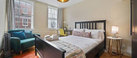 A bedroom with a bed, a chair, a lamp, and a heater.