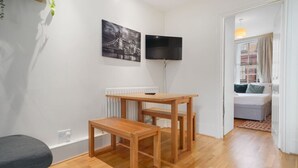 A room with a wooden table, a TV mounted on the wall, and a bed with a view of the street. - 2-BR in the Heart of Soho - 5 guests (Greater London)