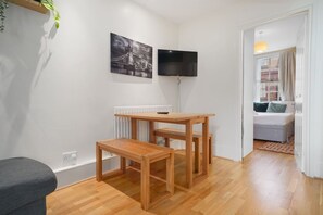 A room with a wooden table, a TV mounted on the wall, and a bed with a view of the street. - 2-BR in the Heart of Soho - 5 guests (Greater London)