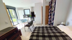 Een slaapkamer met een geruit sprei, een houten dressoir, een zithoek met een tafel en stoelen, en een kitchenette met een magnetron en fornuis.
