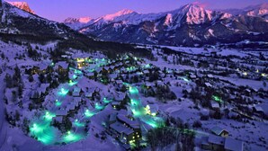 Een besneeuwd dorpje met gebouwen die verlicht zijn met groene lichten, omgeven door bergen.