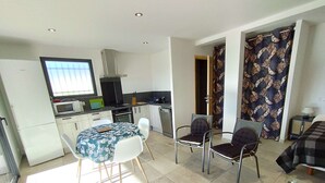 Een ruimtelijk ingerichte leefruimte met kitchenette, eethoek en slaapkamer.