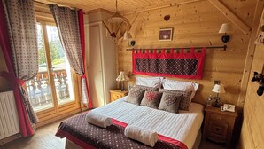 Un dormitorio de cabaña de madera con cama, cortinas, ventana, lámpara de pared y una mesita de noche pequeña.