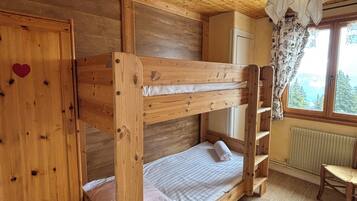 Habitación con literas, techo de madera, armario decorado con un corazón, radiador y ventana con vistas.