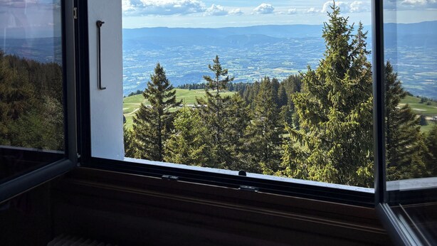 Una habitación con un amplio ventanal que ofrece vistas a un paisaje boscoso y montañas distantes.