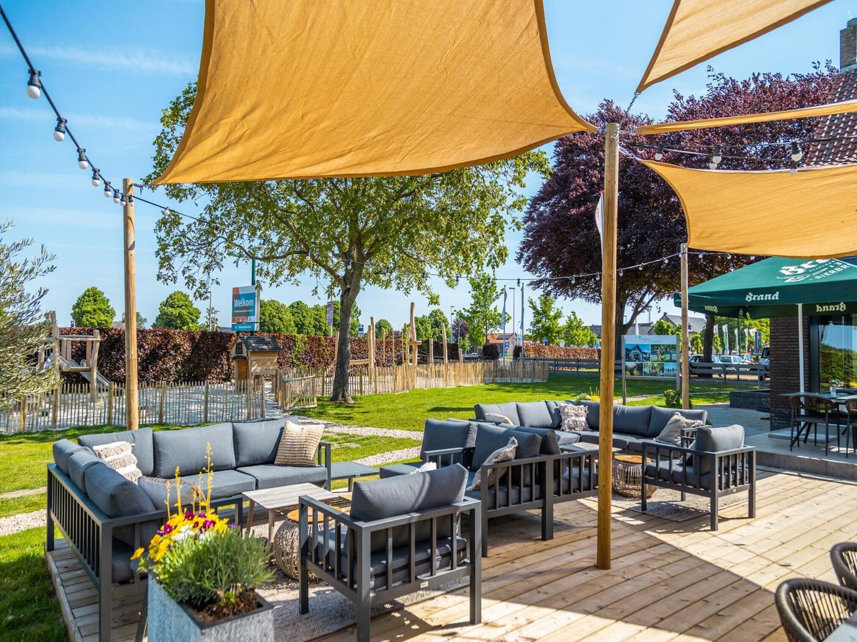 Een terras met meerdere banken en tafels, een houten dek en een 'Welcome'-bord op de achtergrond.