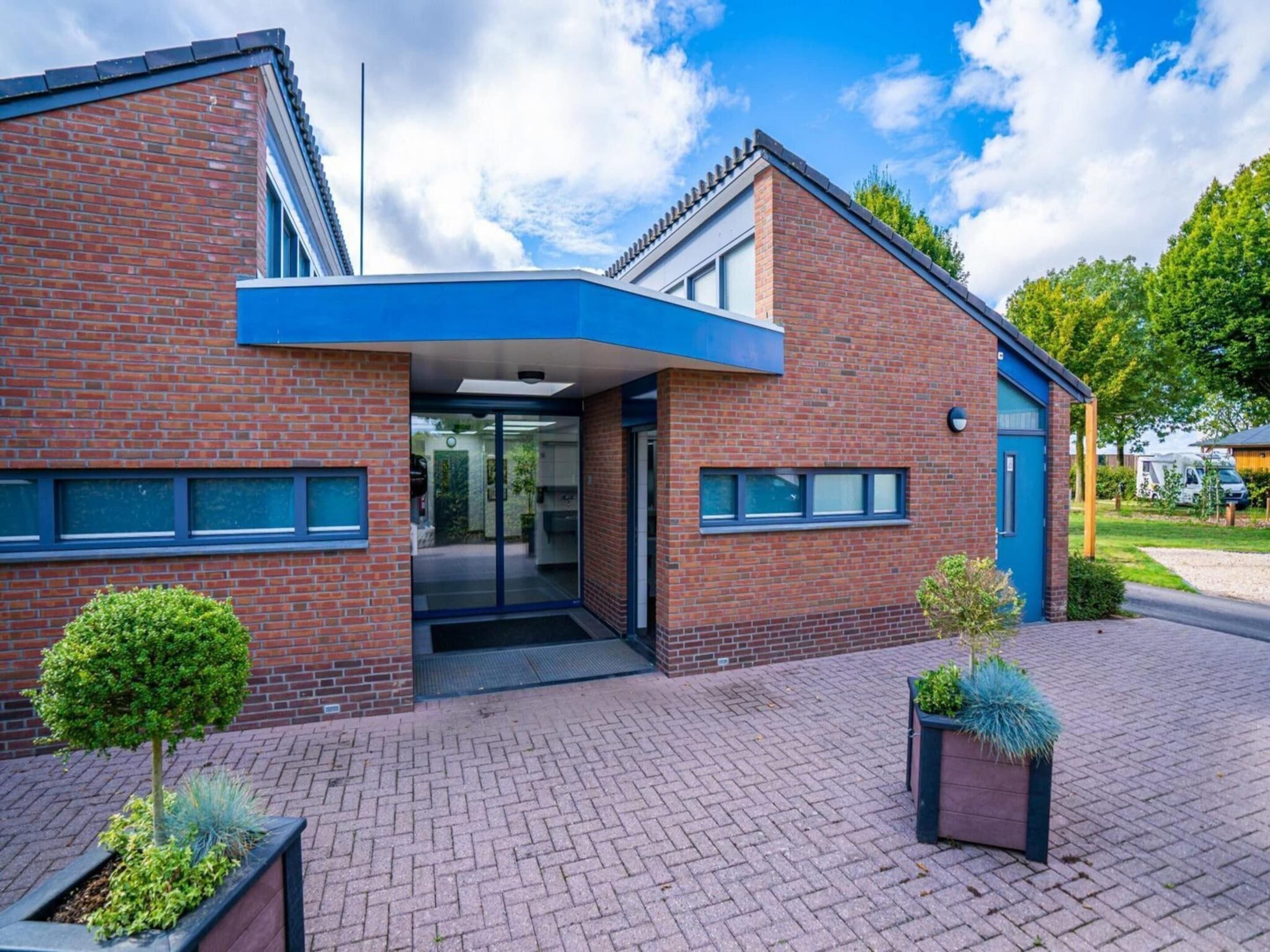 Een modern gebouw met een bakstenen gevel, een glazen entree en een blauw dakoverhang.