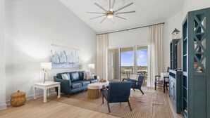 A spacious living room with a blue sofa, a coffee table, a ceiling fan, and a view of the outdoors. - Newly remodeled top floor gem in Cinnamon Beach condo 1062! (Palm Coast)