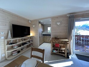 Ein gemütliches Wohnzimmer mit Fernseher, Holzböden und einem Essbereich.