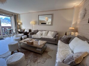 A modern living room with a grey sofa, white fluffy poufs, a coffee table, and a large mirror on the wall. - Spacious apartment, parking included - 8 guests (Méribel)