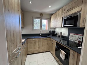 A modern kitchen with wooden cabinets, a black countertop, stainless steel appliances, and a window with a view of trees. - Spacious apartment, parking included - 8 guests (Méribel)