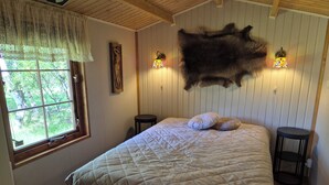 Un dormitorio con una cama grande, dos mesitas de noche, una ventana con vistas a árboles, una alfombra de piel en la pared y dos apliques.