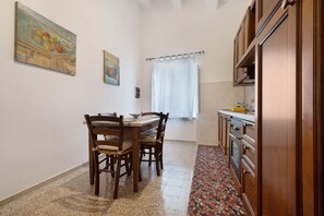 A compact kitchen with wooden cabinets, a dining table with chairs, and a tiled floor.