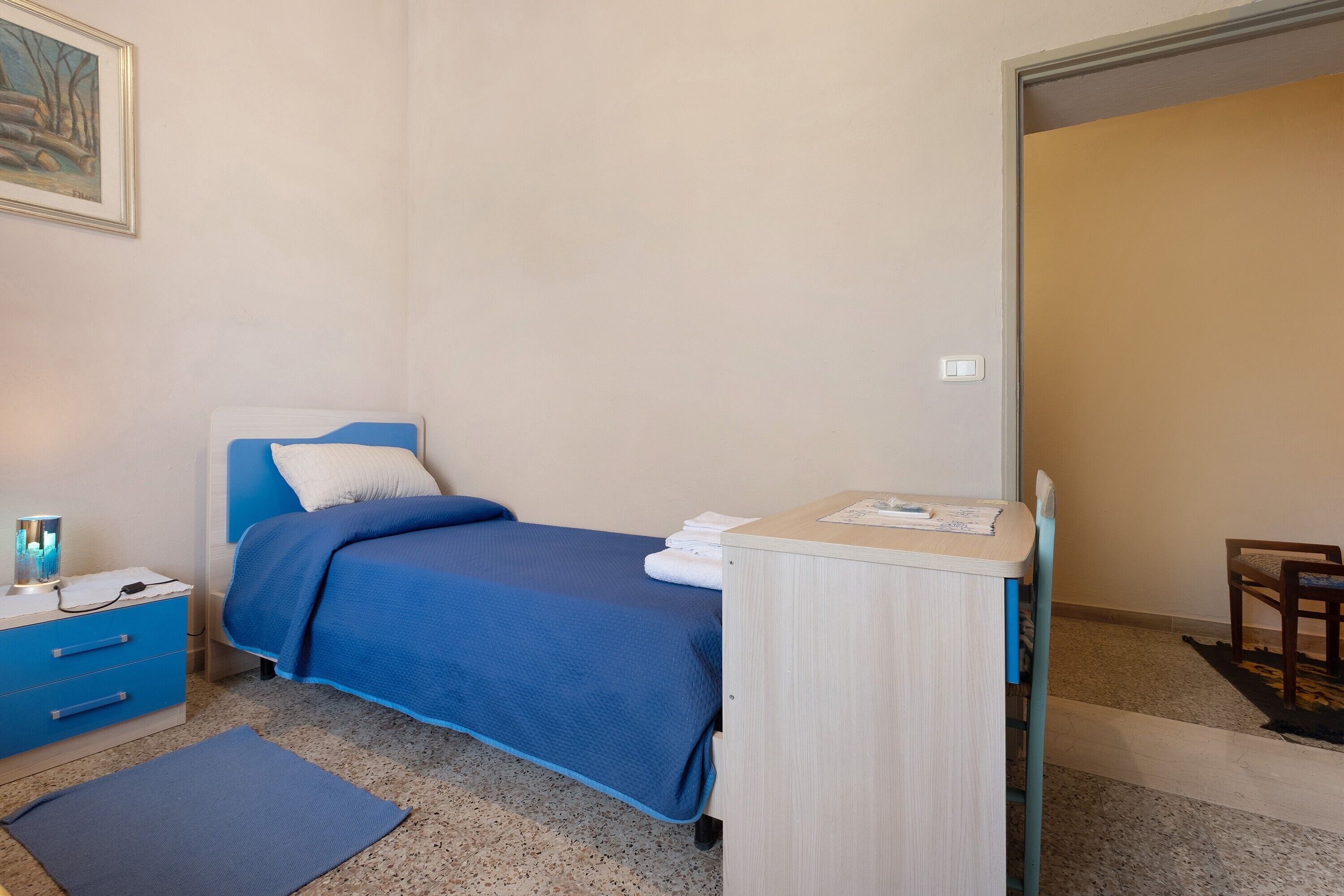 A bedroom with a bed, a bedside table, a lamp, a chair, and a door.