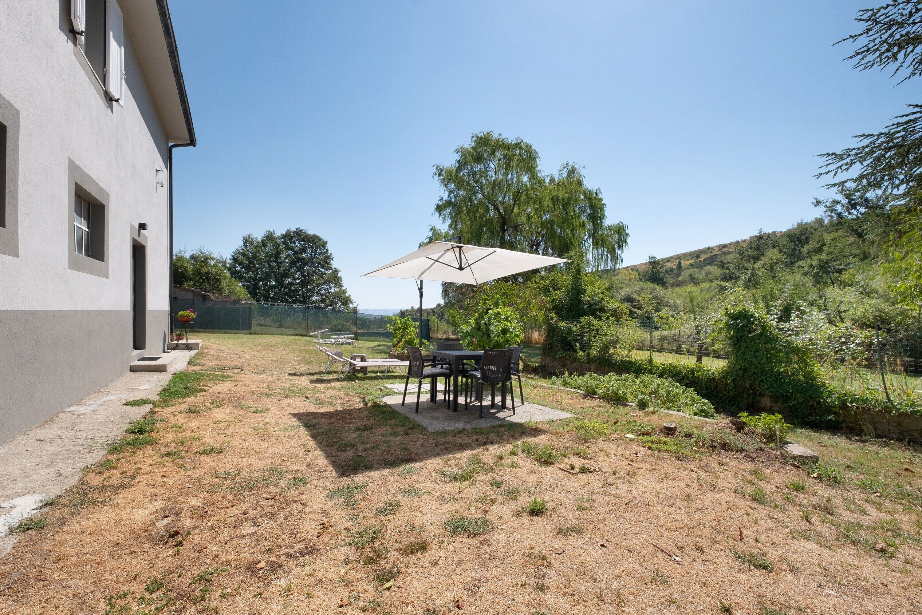 A patio area with a table and chairs, a covered seating area, and a view of a hilly landscape.