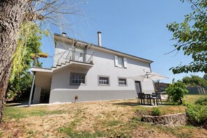 A two-story house with a balcony, a small garden, and outdoor furniture.