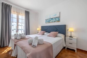 A hotel room with a bed, two bedside tables, a nightstand, a window with curtains, and a painting on the wall. - Can Llorenç - Encanto costero cerca de la playa (Port de Pollença)