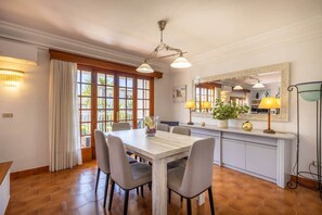 A dining area with a wooden table, four chairs, a vase with flowers, and a large mirror above the counter. - Can Llorenç - Encanto costero cerca de la playa (Port de Pollença)