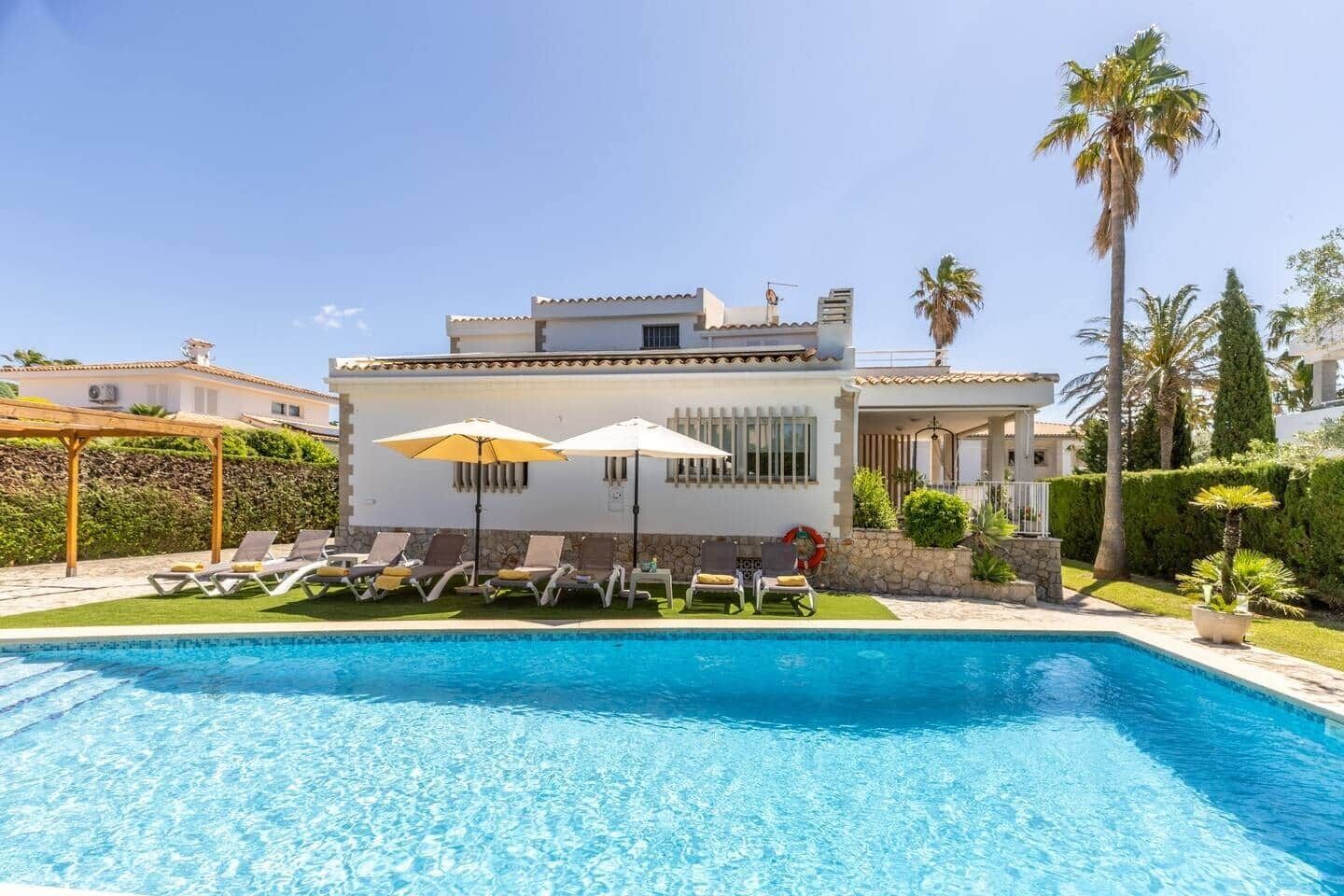 A modern villa with a swimming pool, sun loungers, and umbrellas.